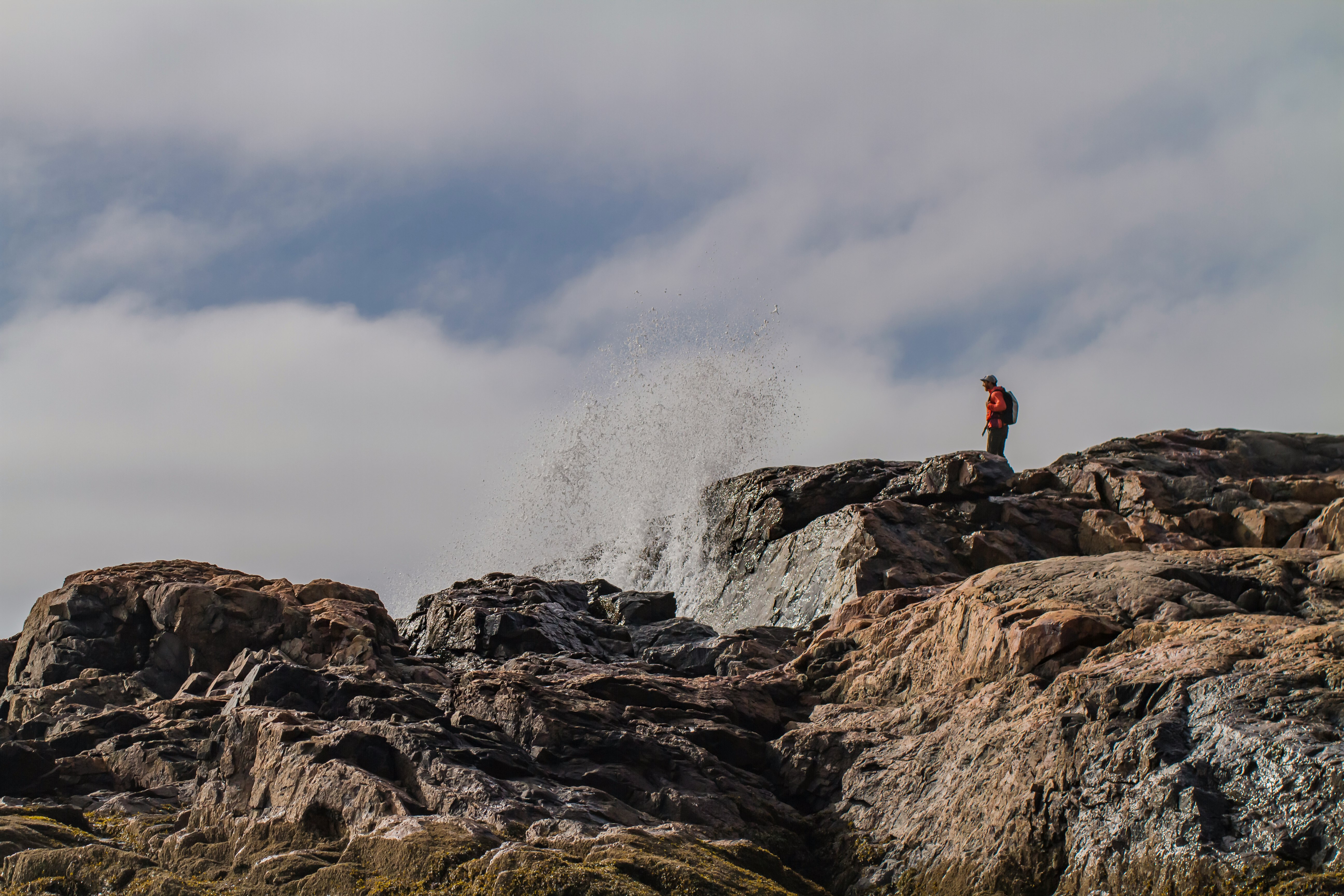 person in red jacket sitting on rock near water falls during daytime